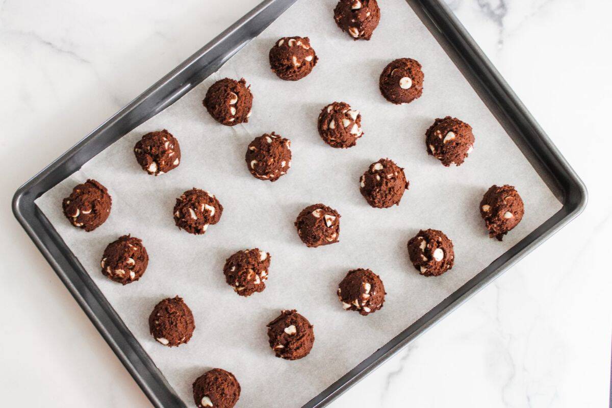 Scooped cookie batter mixture placed on parchment paper in a baking pan, ready to bake.