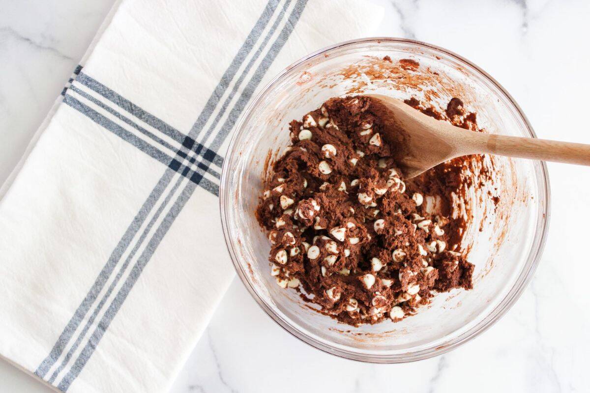 Chocolate cookie mixture with white chocolate chips in a large bowl, with a spatula resting on top.