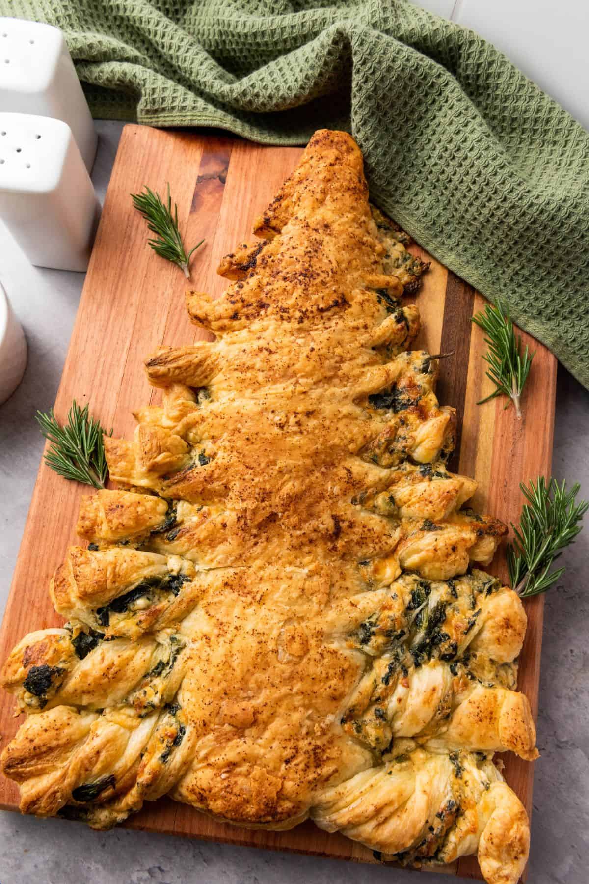 Christmas tree–shaped spinach pastry on a serving board, golden and flaky, garnished with fresh herbs.