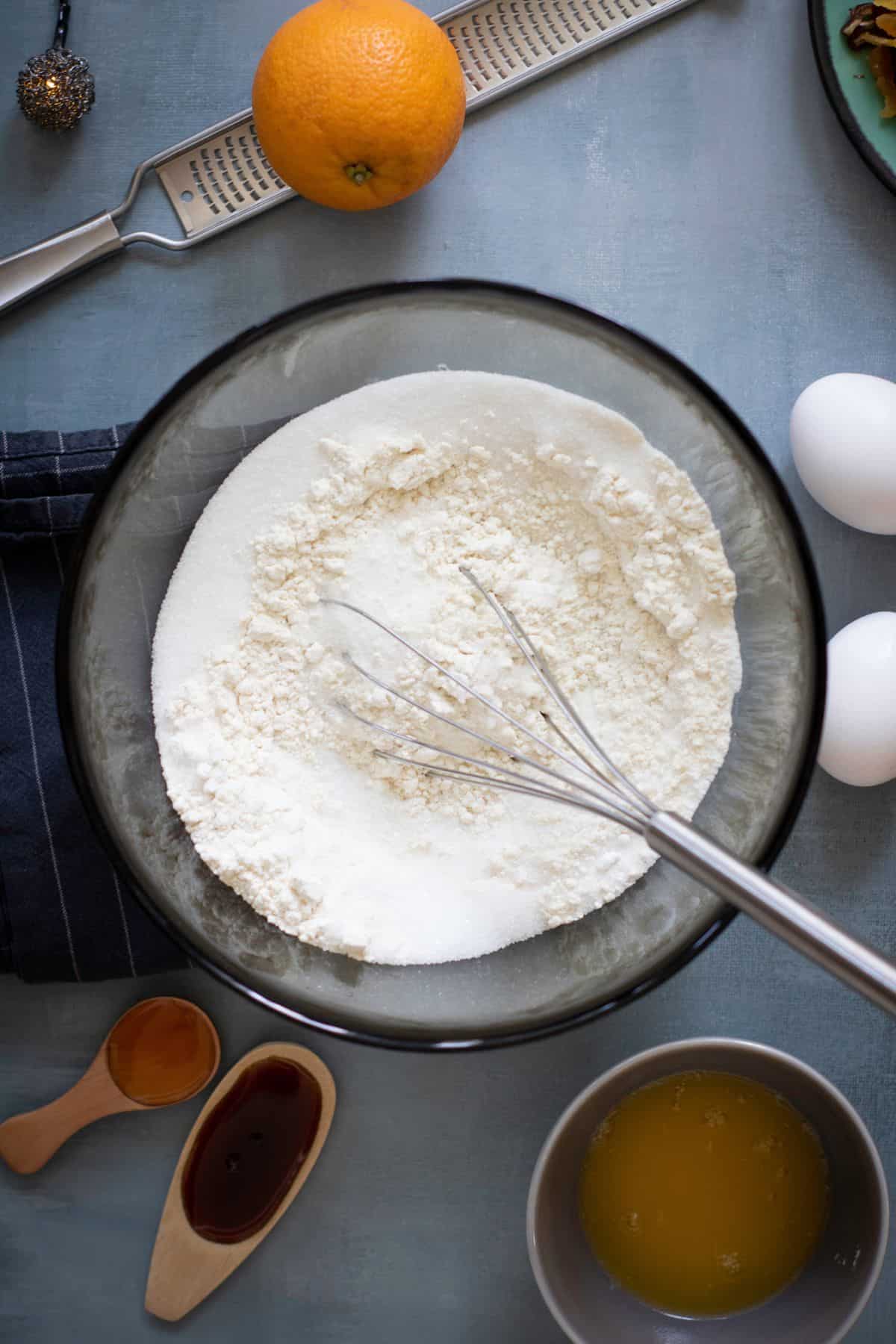 Dry ingredients mixed in a large bowl with a whisk resting on it, surrounded by other ingredients on the surface.