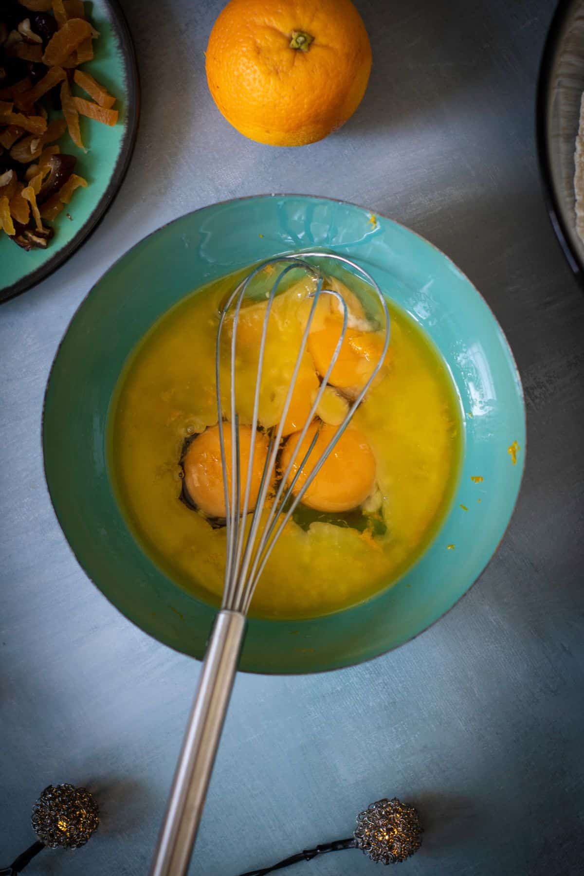 Wet ingredients mixed in a bowl with a whisk resting on it, surrounded by other ingredients on the surface.