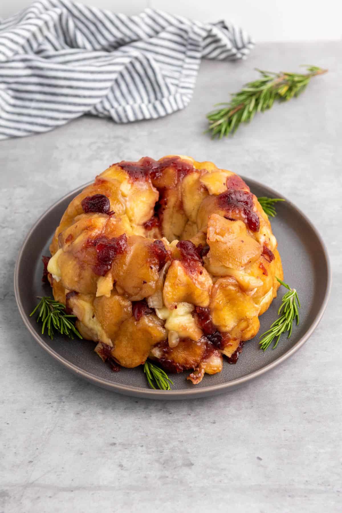 Mini cranberry brie pull-apart bread arranged on a plate and garnished with fresh cranberries and herbs.