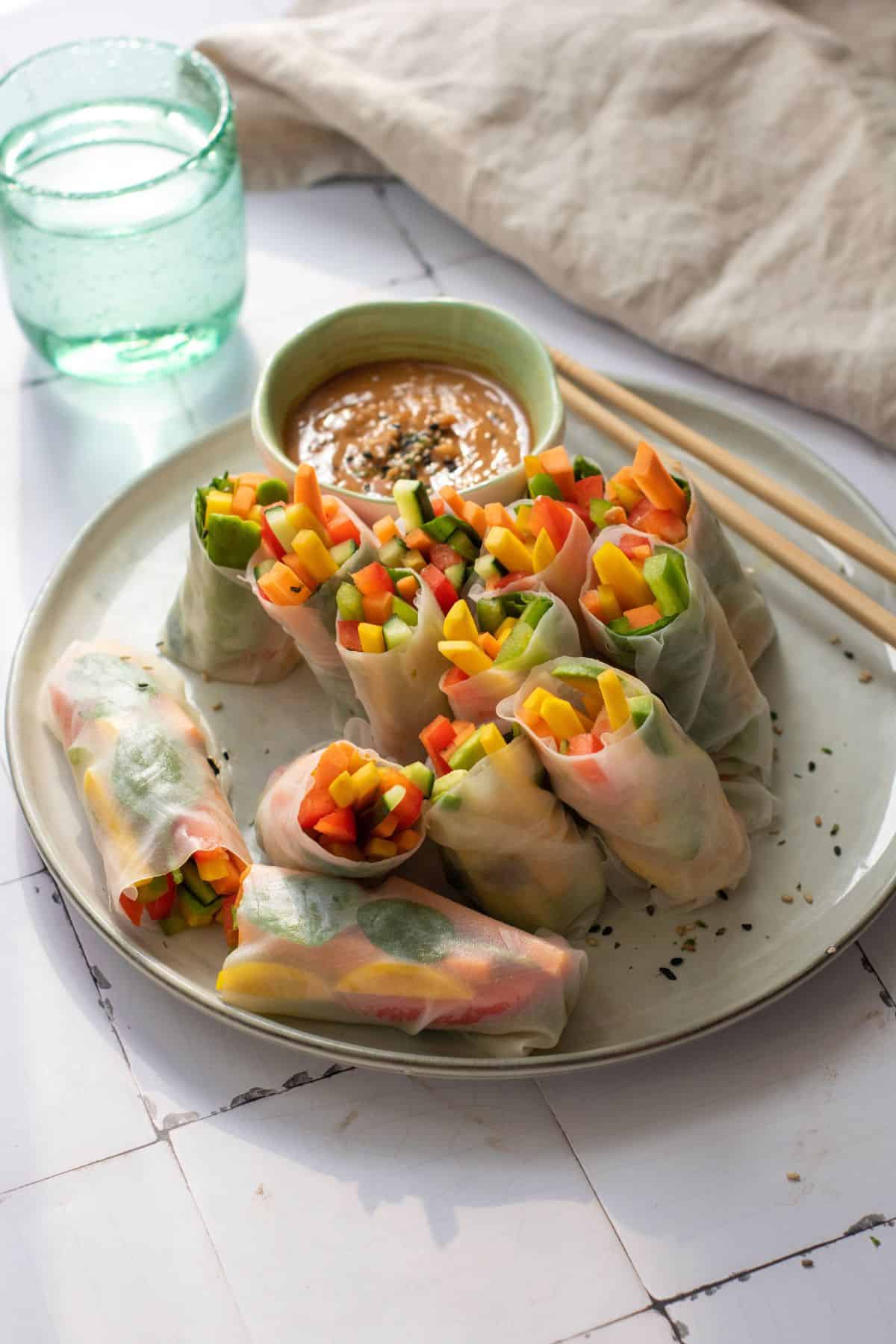 A plate of rainbow vegetable rolls served with a dipping sauce and a pair of chopsticks.
