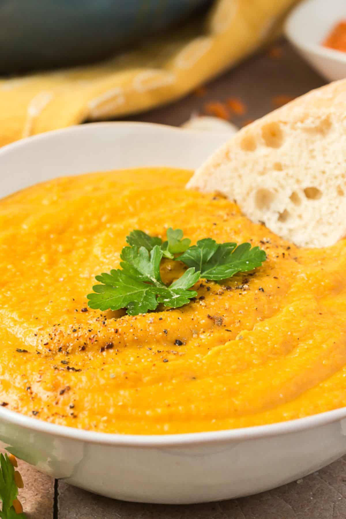 Close-up of a bowl of lentil soup with a piece of garlic bread resting on the edge.