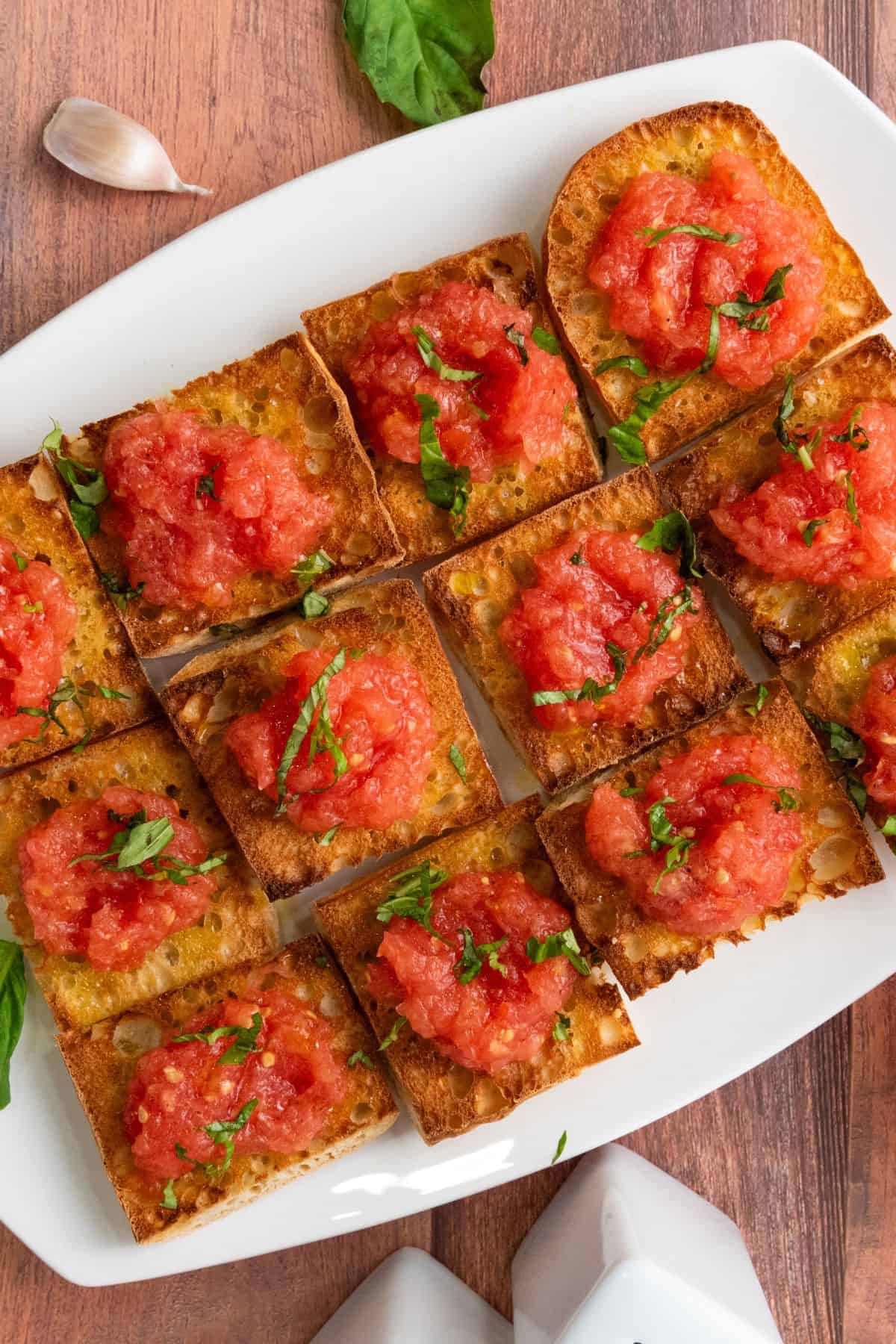 Spanish pan con tomate tapas arranged on a plate, topped with grated tomato, a drizzle of olive oil, and a sprinkle of salt.