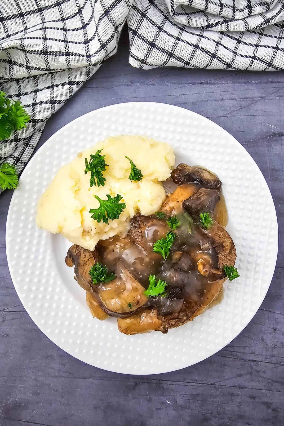 Crockpot Chicken Marsala served with mashed potatoes on a plate with cloth underneath.