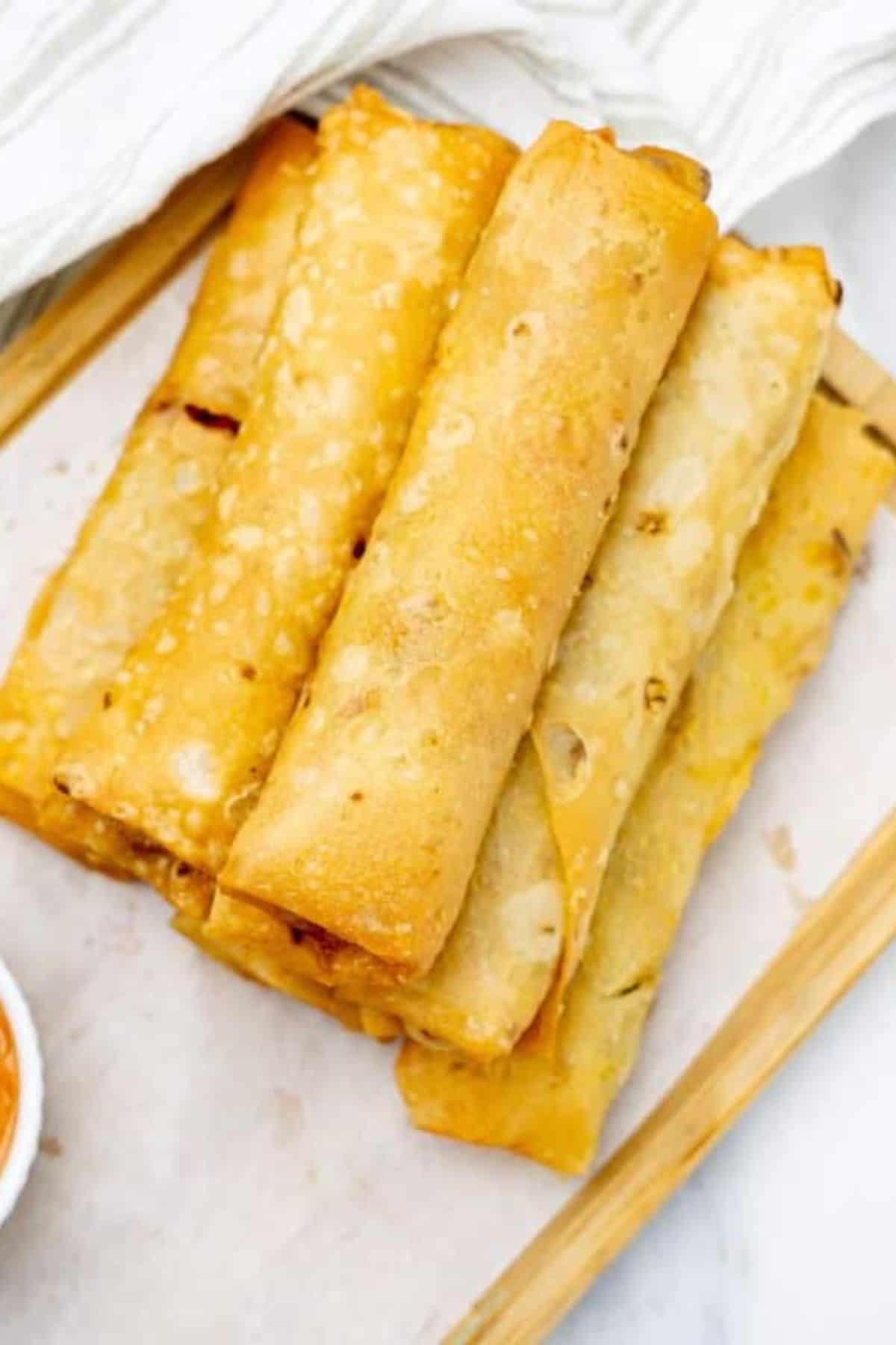 Chicken and Vegetable Spring Rolls served on a wooden board with dipping sauce.