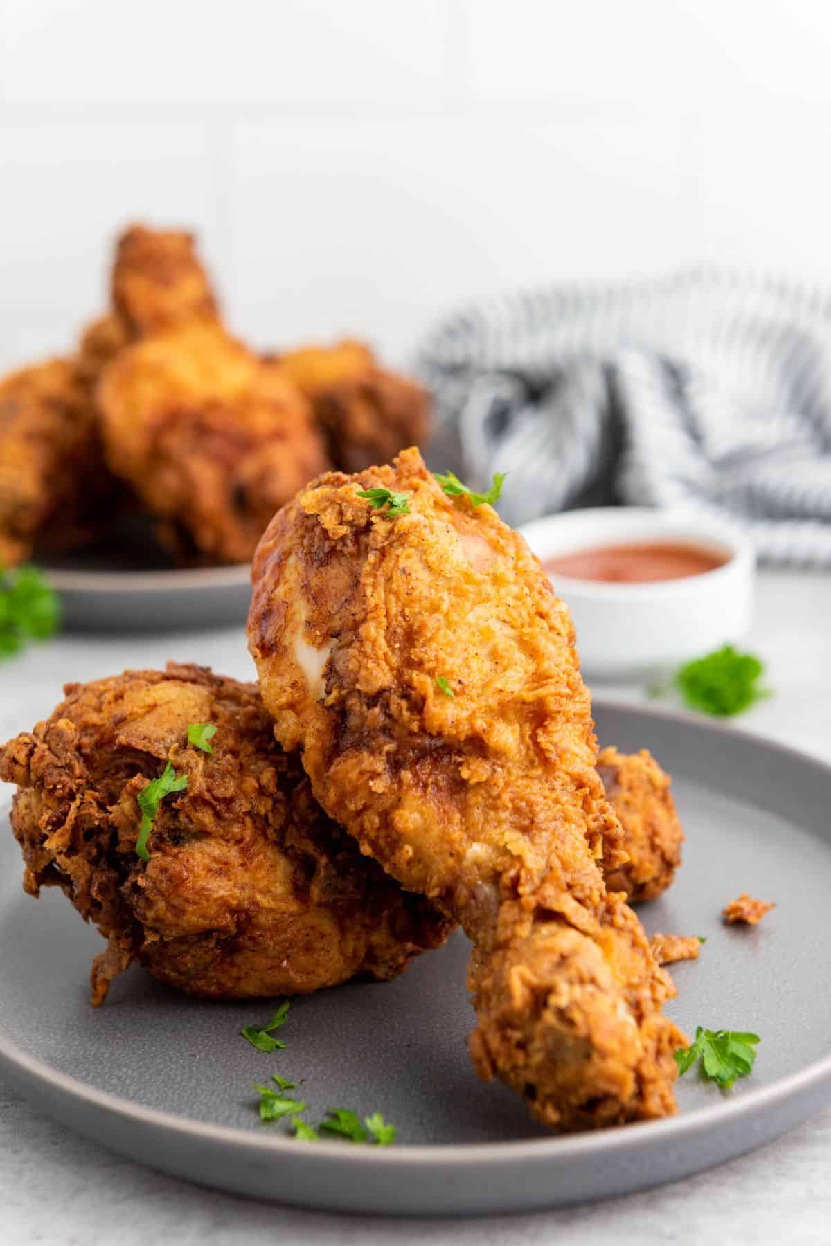 Crispy buttermilk fried chicken served on a plate with dipping sauce, with more chicken in the background.