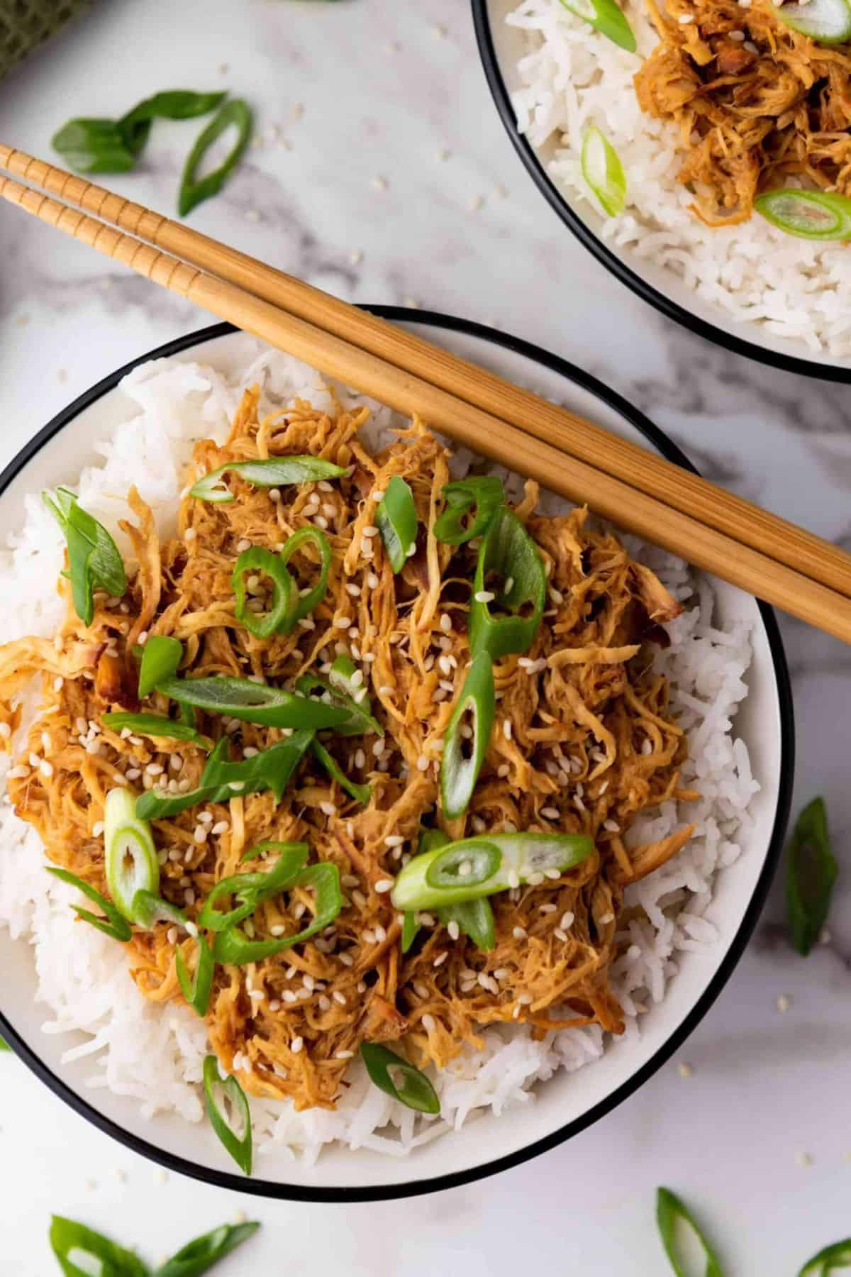 A bowl of rice topped with Crockpot Slow Cooker Soy Honey Garlic Chicken, served with chopsticks.