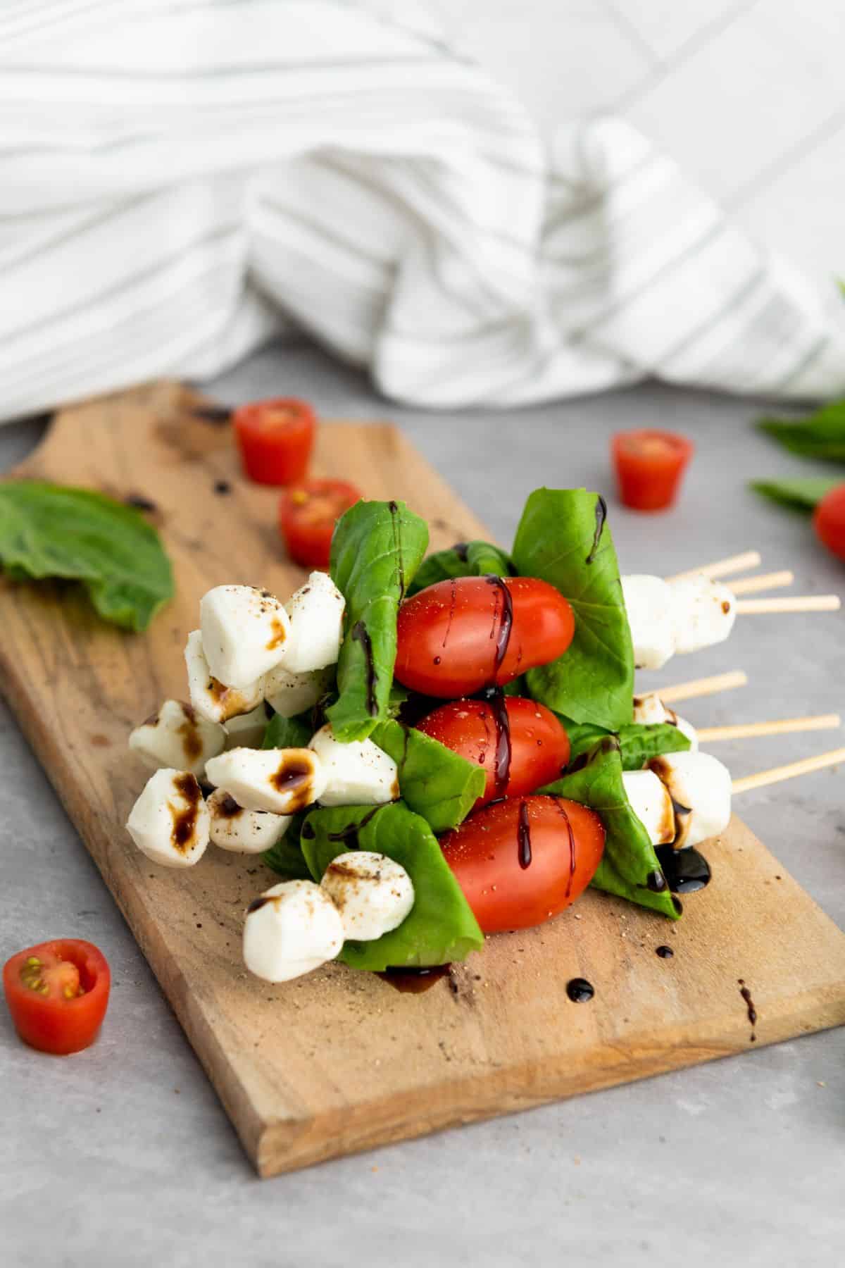 Stack of flavorful caprese salad skewers arranged on a wooden board, surrounded by cherry tomatoes with a table napkin on the side.