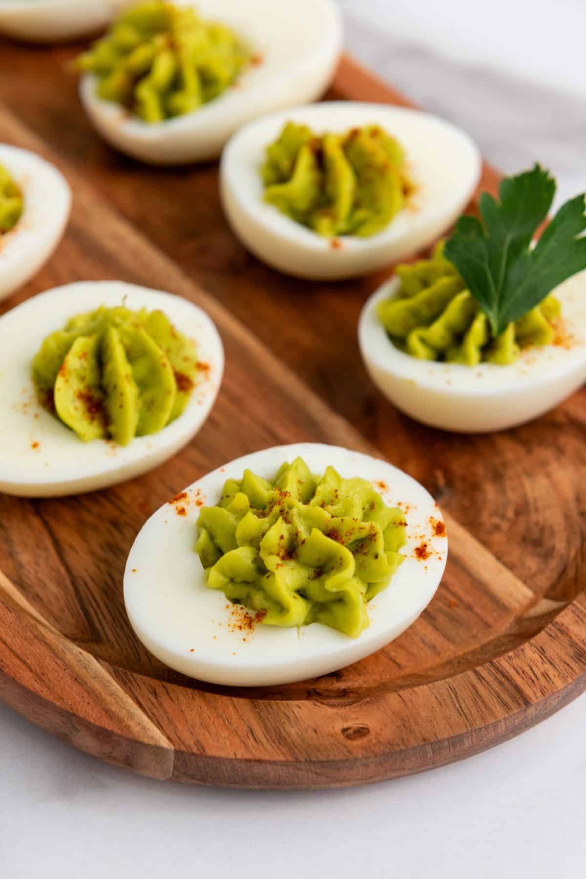Close-up of loaded avocado deviled eggs on a plate, topped with a sprinkle of paprika and fresh herbs.