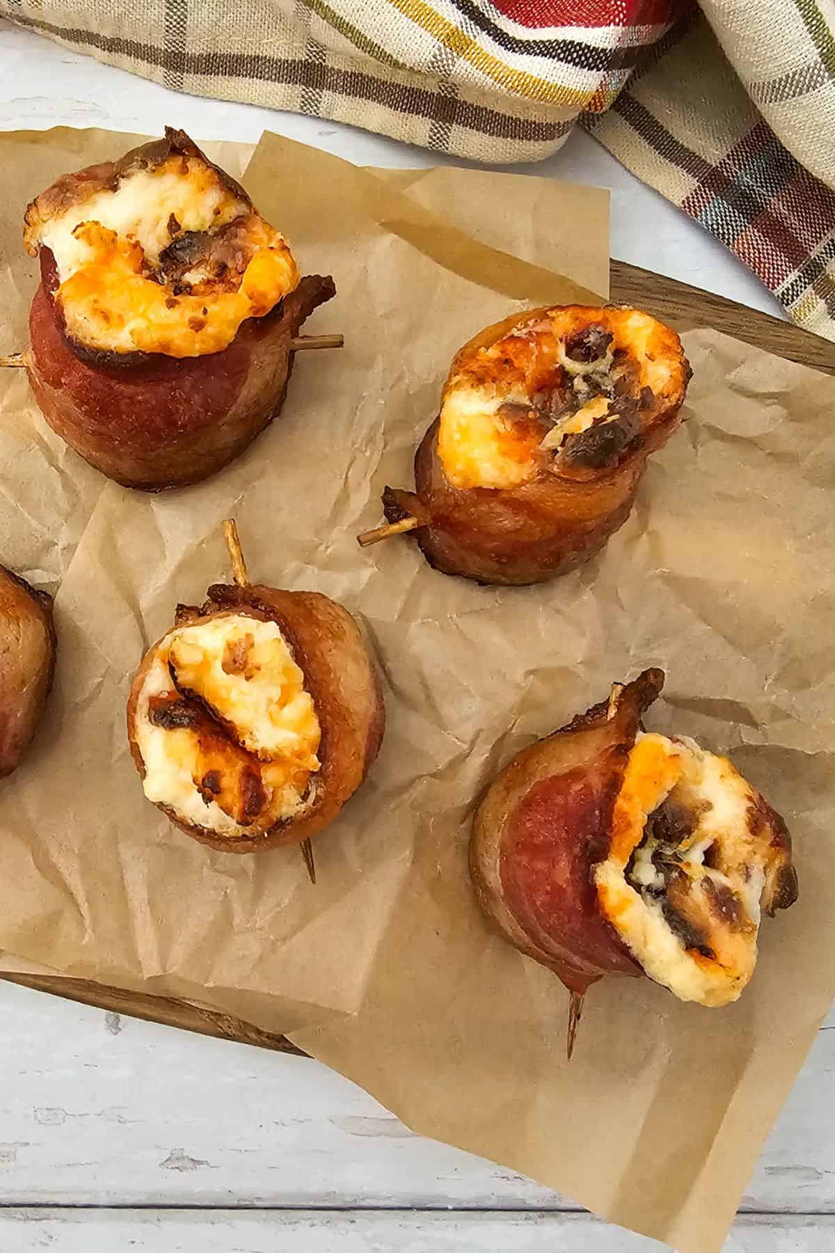 Air fryer pig shots arranged on parchment paper, showing crispy bacon-wrapped sausages stuffed with melted cheese.