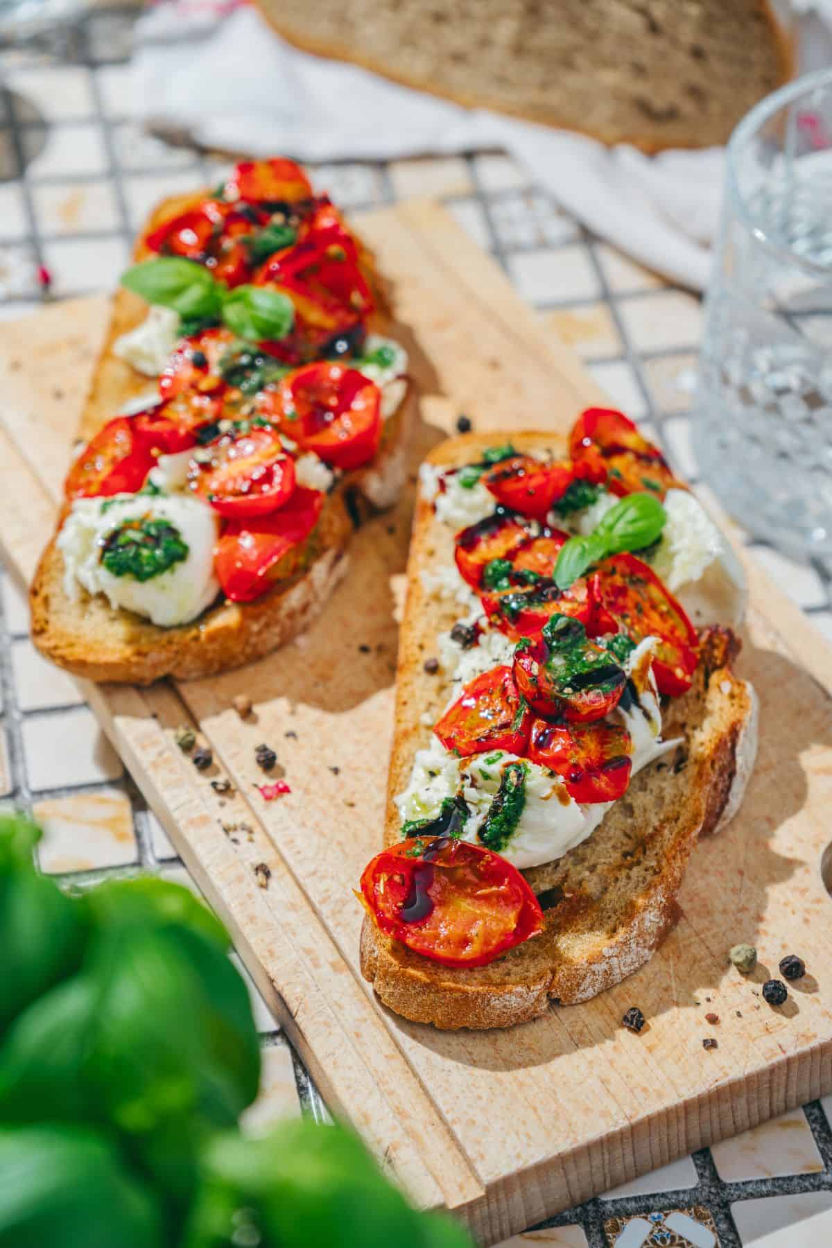 Savory burrata toast with roasted tomatoes & basil drizzle on a wooden board, garnished with fresh basil.