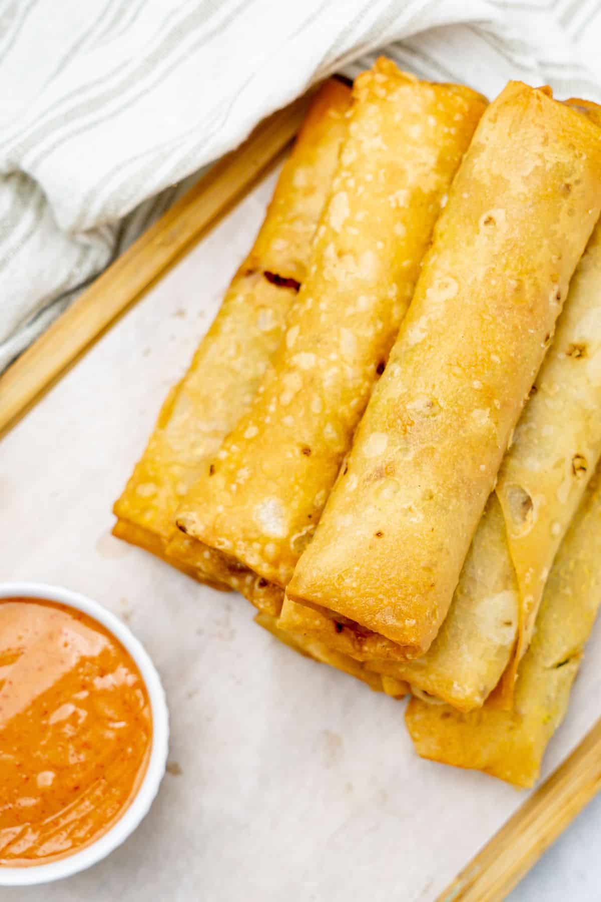 Chicken vegetable spring rolls on a wooden board with dipping sauce.