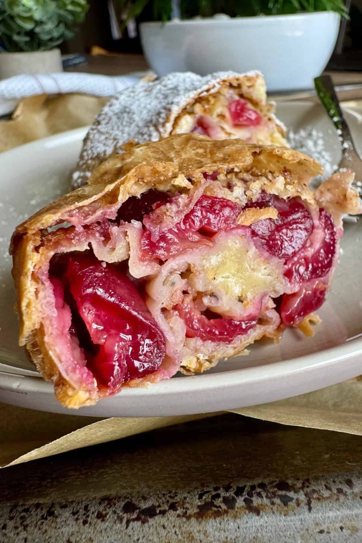 Close-up of a simple cherry strudel on a plate, showing the cherry filling inside the flaky pastry.