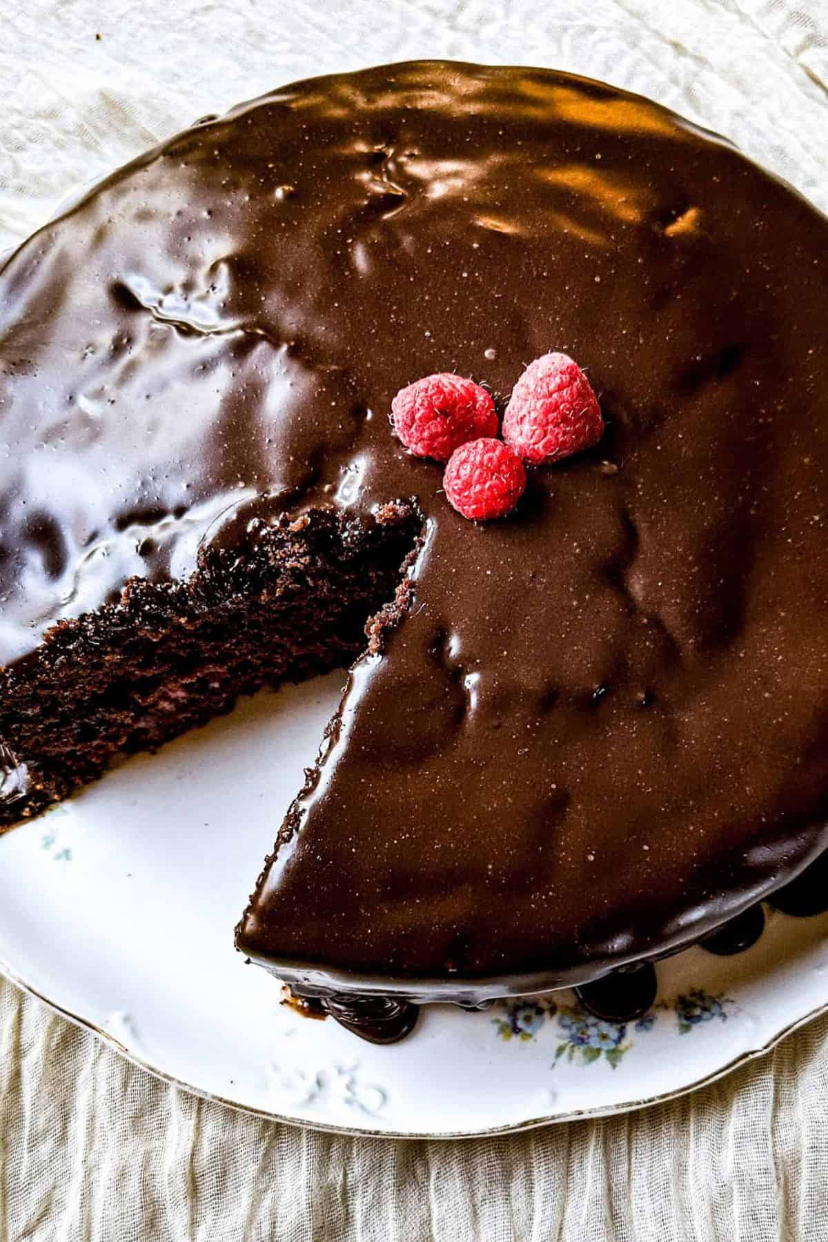 A slice of chocolate cake topped with fresh raspberries, with the remaining cake visible in the background.