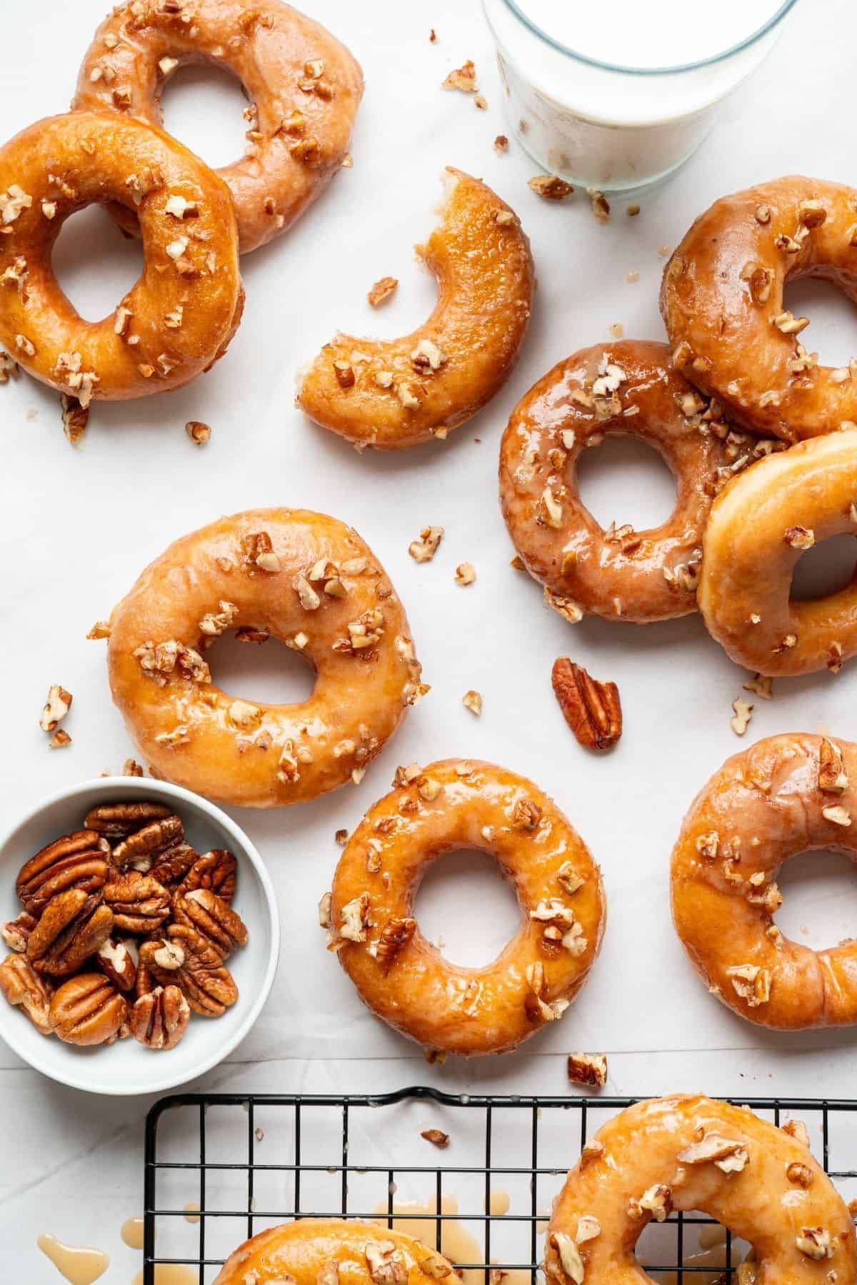 Maple glazed donuts arranged on a surface, surrounded by scattered nuts.