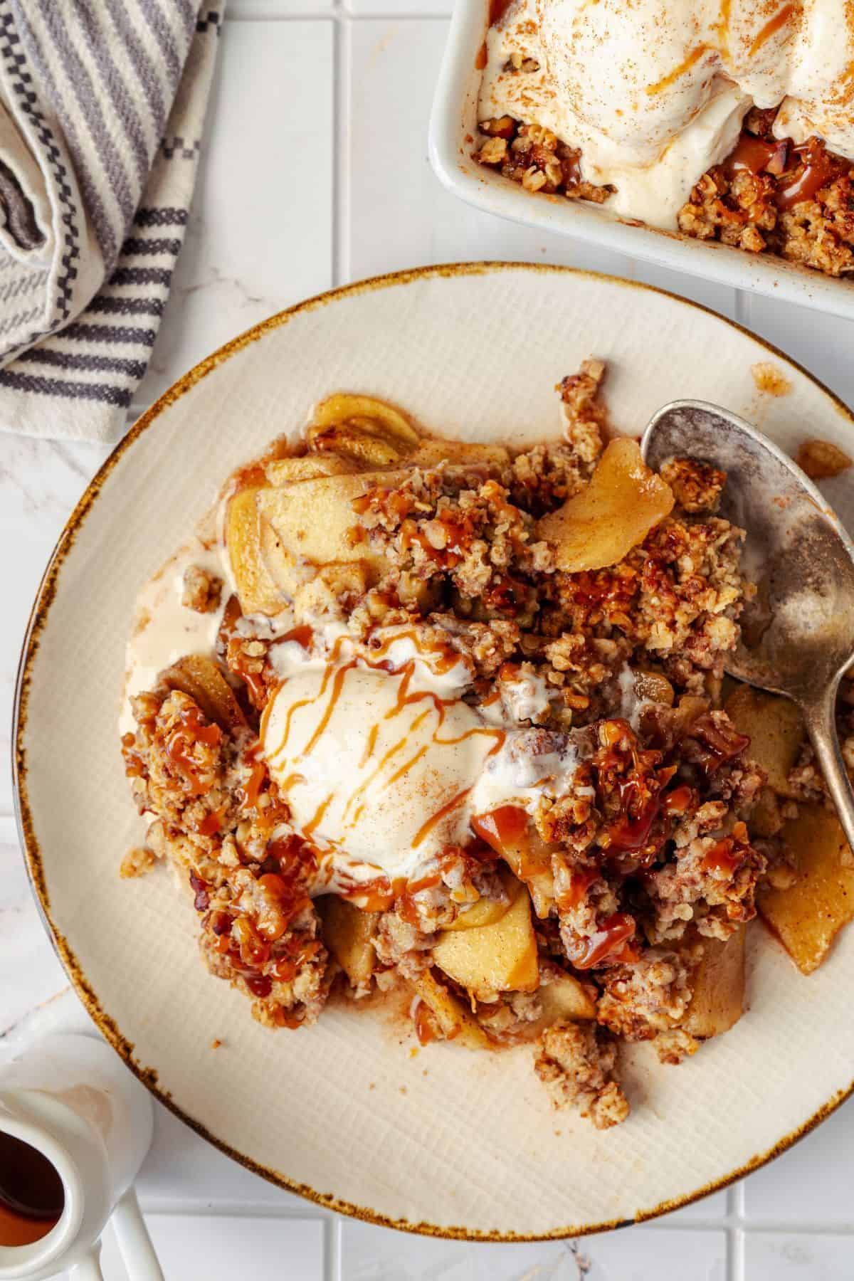 Caramel apple crisp served on a plate, topped with a scoop of vanilla ice cream.