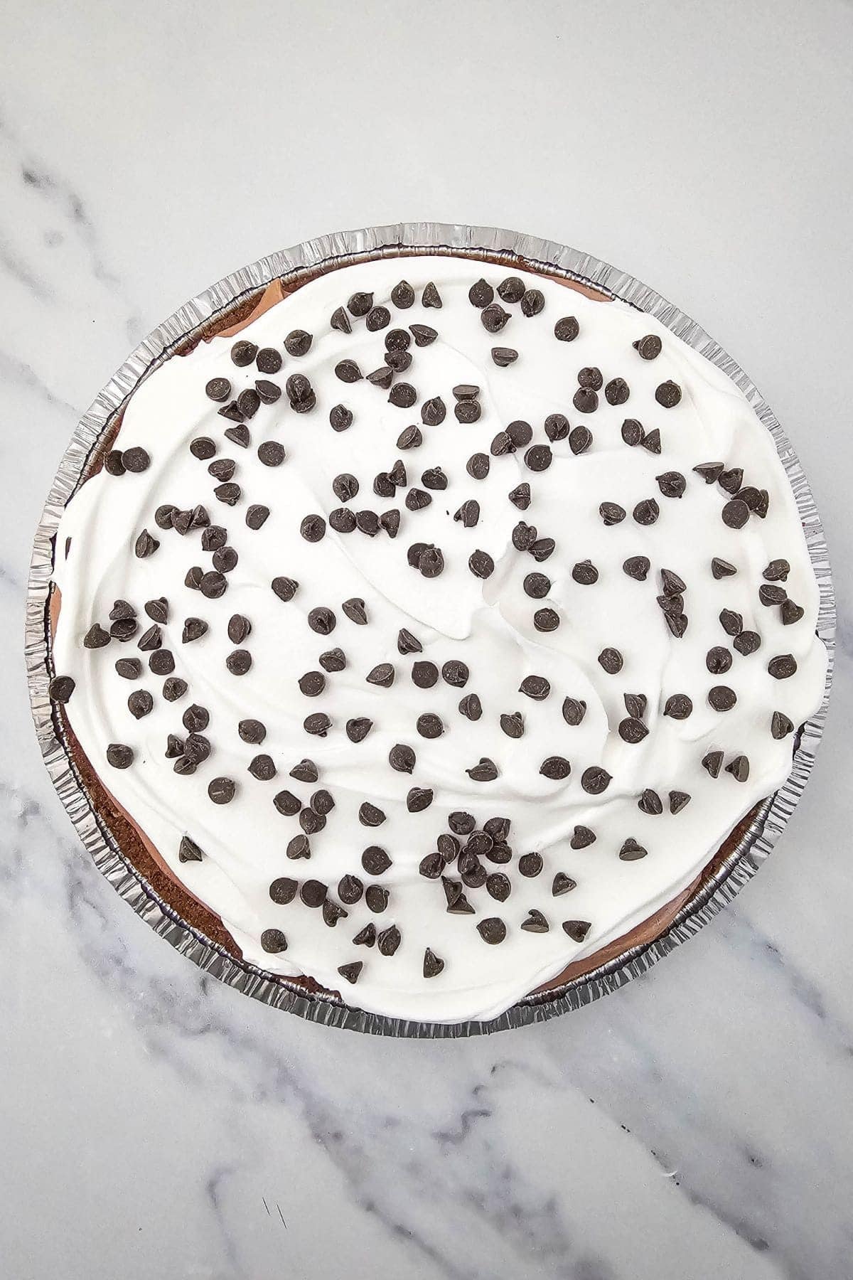 Chocolate pudding pie on a marble surface, topped with whipped cream and chocolate kisses.
