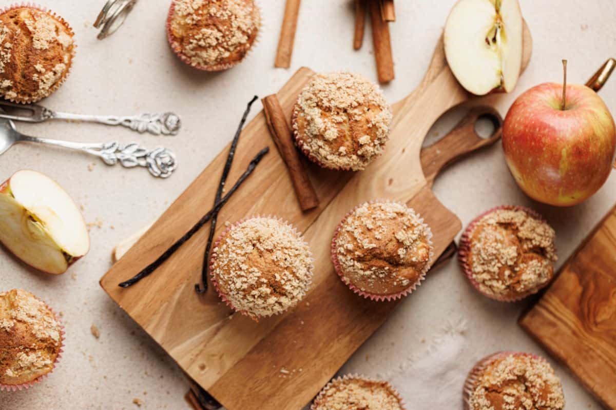 Apple cinnamon muffins served on a wooden board, garnished and accompanied by fresh apple.