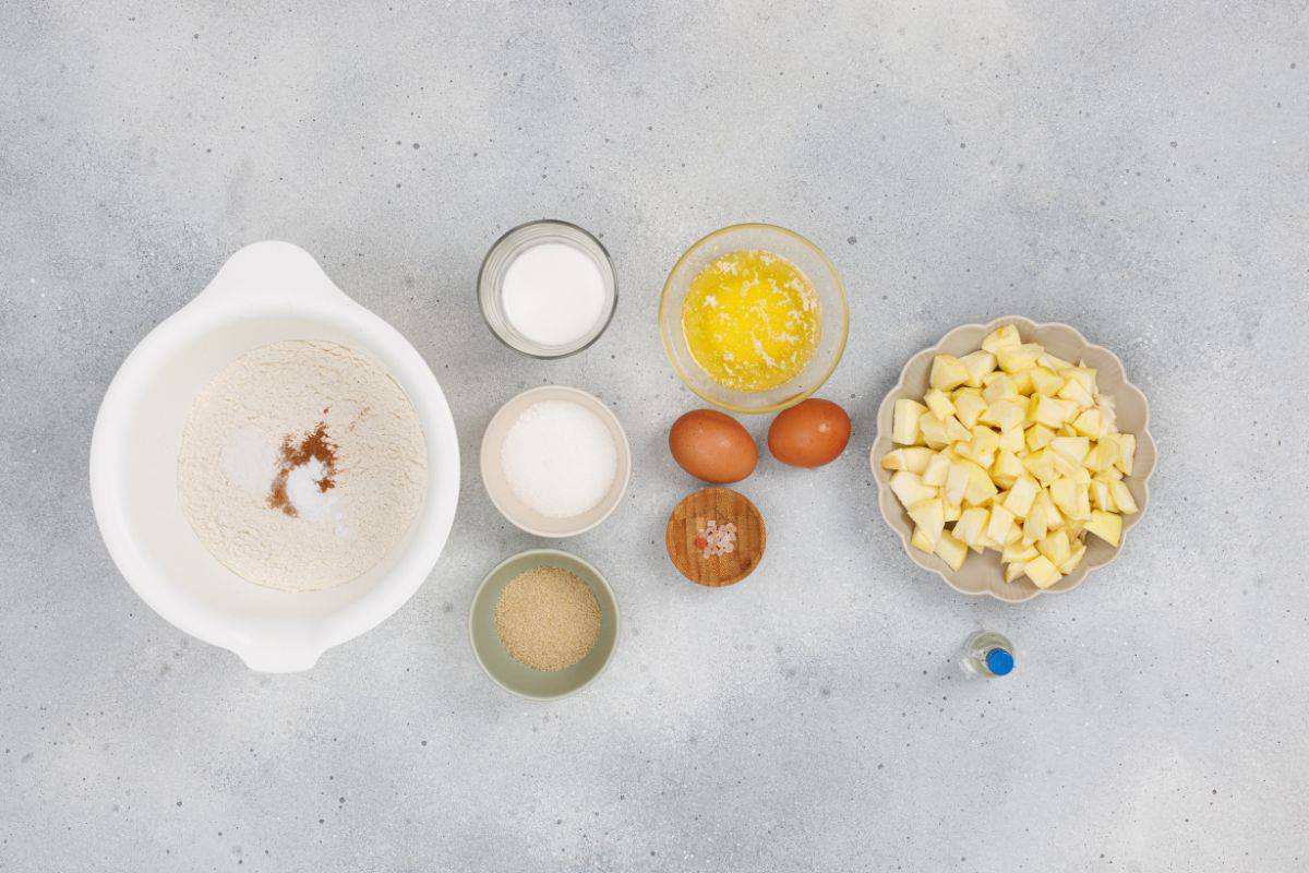 Ingredients for apple cinnamon muffins mixed in a large bowl, surrounded by other ingredients on the surface.
