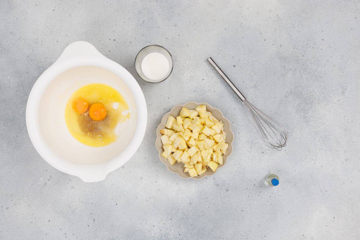 Large bowl with wet ingredients being mixed and a small bowl with diced apples and a whisk on the surface.