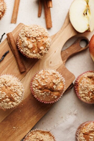Apple cinnamon muffins served on a wooden board, garnished and accompanied by fresh apple.