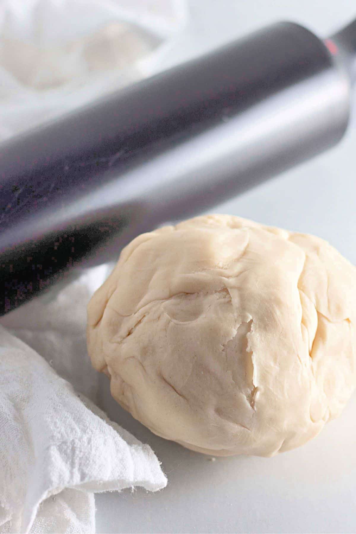 Round pie dough on a surface with a stainless steel rolling pin resting nearby.