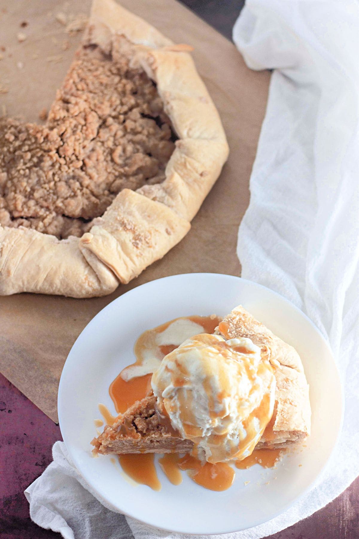 Sliced Apple Crumb Galette served on a plate with a scoop of vanilla ice cream, with the remaining galette visible in the background.