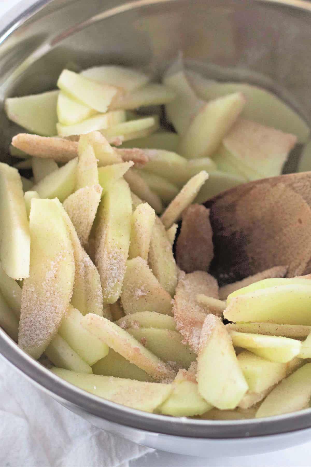 Sliced apples being seasoned and mixed with a spatula in a large bowl.