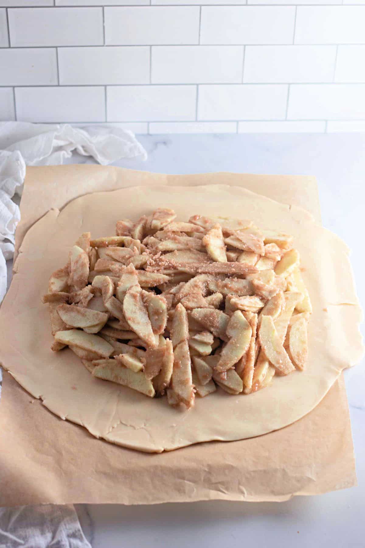 Sliced apples arranged on the rolled-out dough on a wooden board.