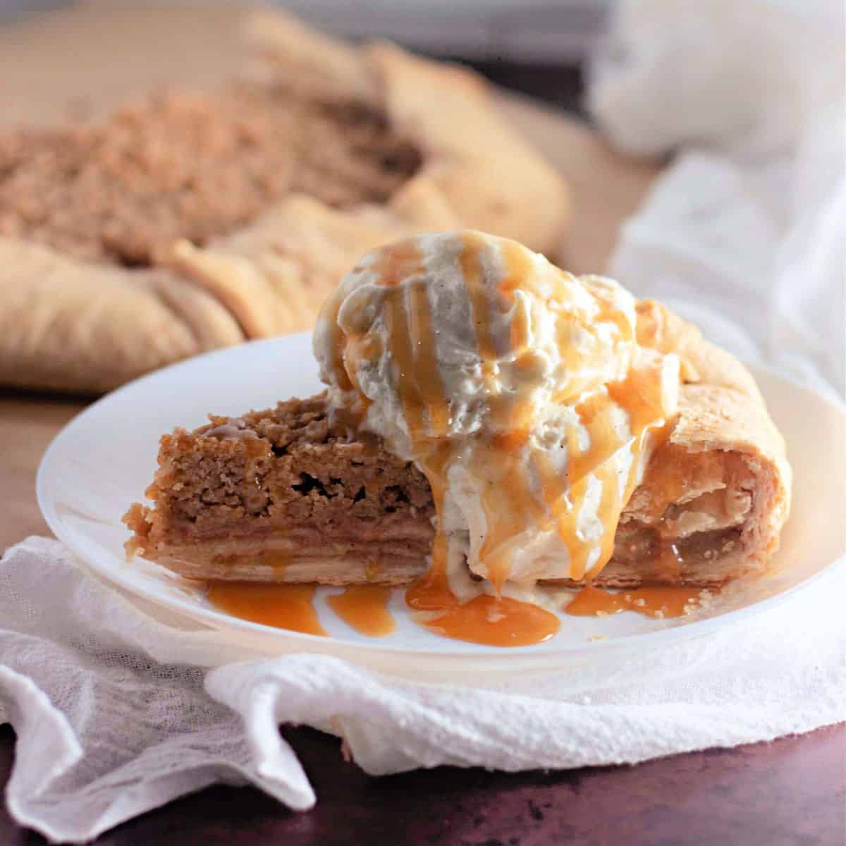 Sliced Apple Crumb Galette served on a plate with a scoop of vanilla ice cream, with the remaining galette visible in the background.