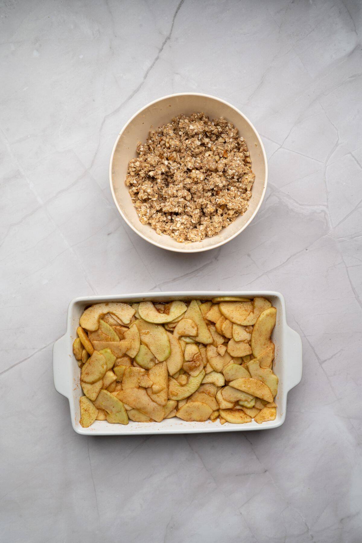 Baking dish filled with apple crisp mixture and a bowl filled with topping ready for baking.