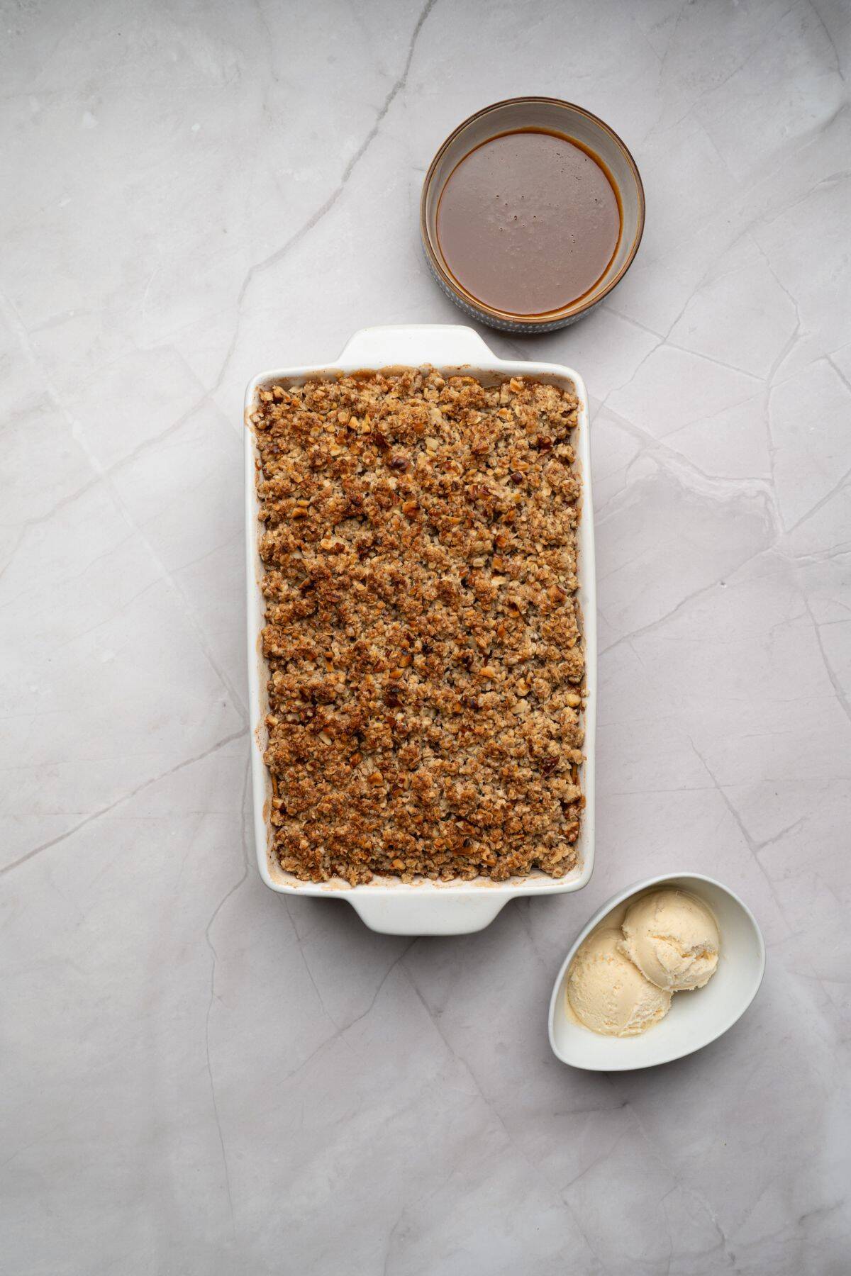 Apple crisp fresh out of the oven in a baking dish with golden oat topping, surrounded by other ingredients.