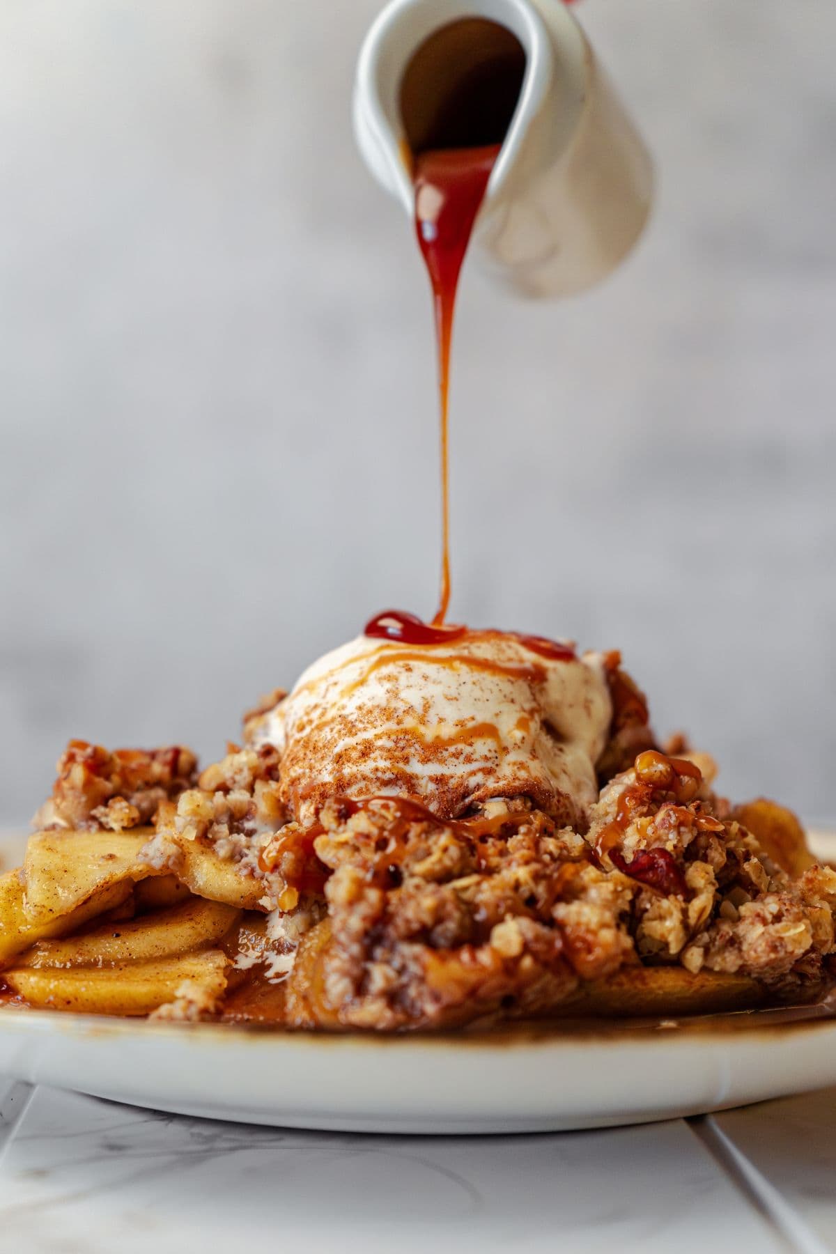 Apple crisp served on a plate, topped with vanilla ice cream and drizzled with caramel sauce.