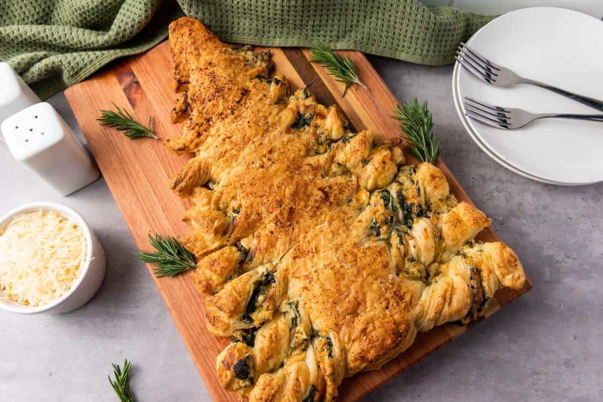 Spinach dip Christmas tree pastry served on a wooden board with festive decorations on the side.