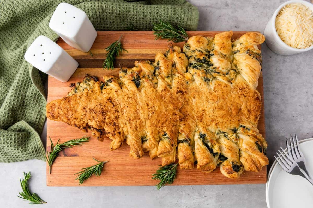 Spinach dip Christmas tree pastry served on a wooden board with festive decorations on the side.