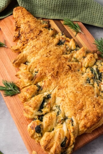Spinach dip Christmas tree pastry served on a wooden board with festive decorations on the side.