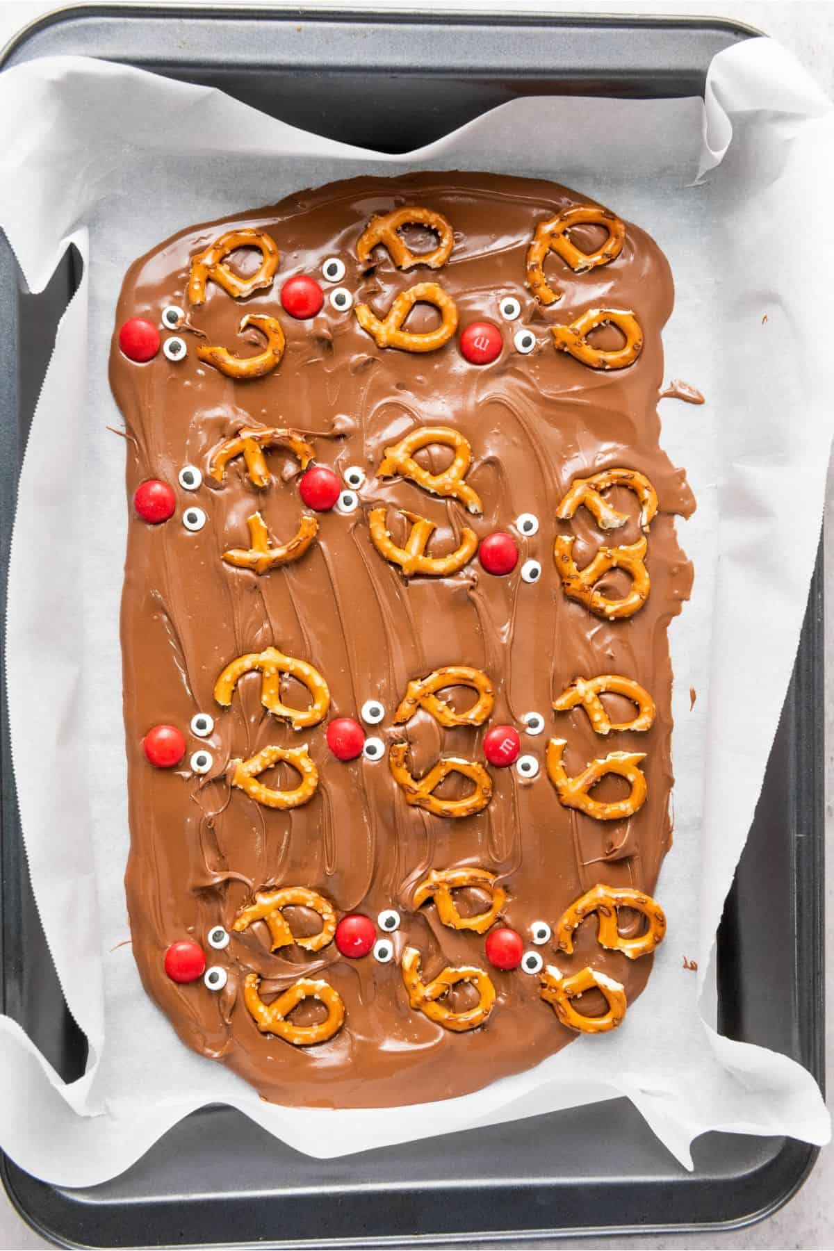 Melted chocolate topped with pretzels and colorful candies in a tray.