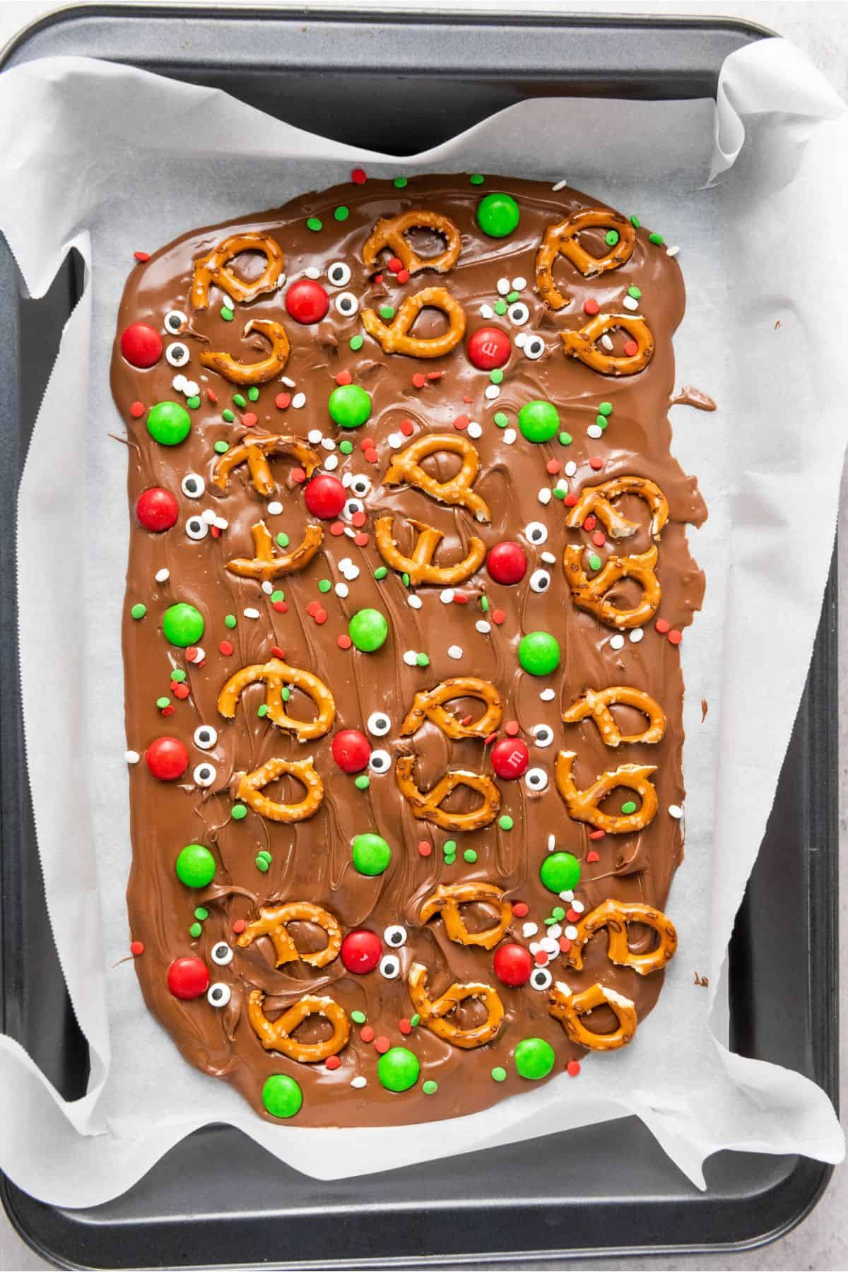 Melted chocolate topped with pretzels and colorful candies in a tray.