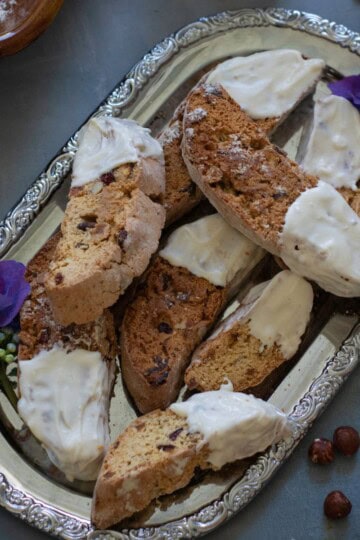 Finished cranberry apricot walnut biscotti dipped in white chocolate, arranged on a decorative tray, garnished with dried cranberries and orange zest.