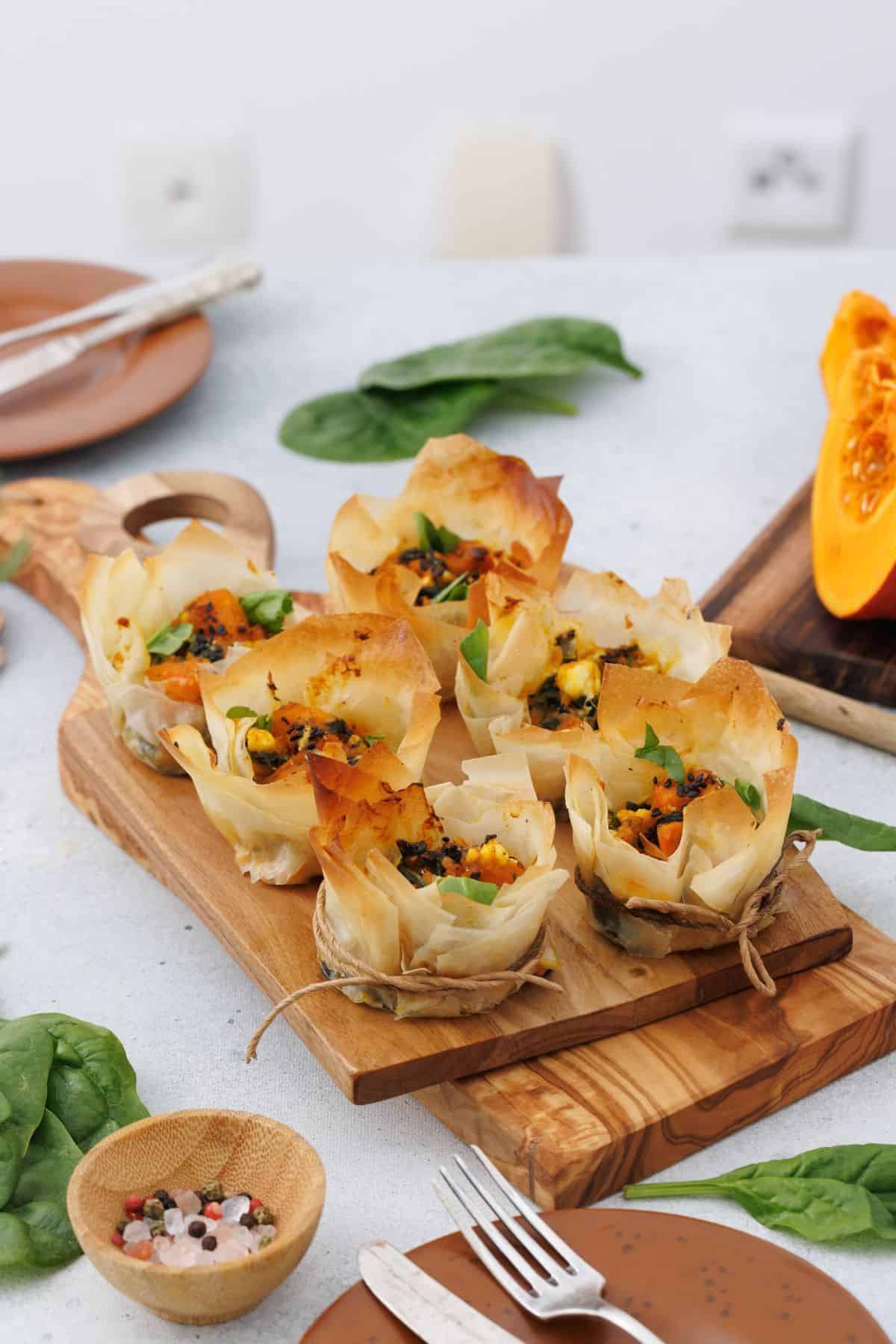Crispy phyllo pastry cups filled with pumpkin and feta, served on a wooden board.