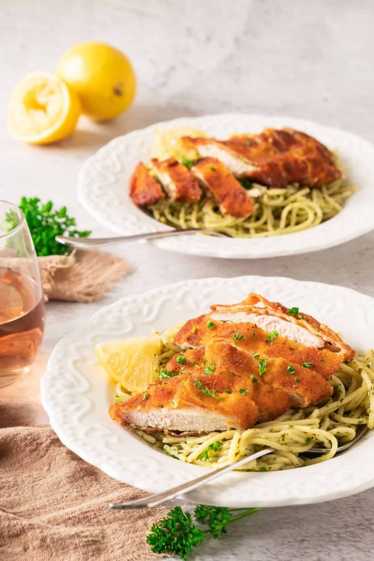 Two plates of spaghetti topped with sliced crispy chicken, garnished with fresh herbs.