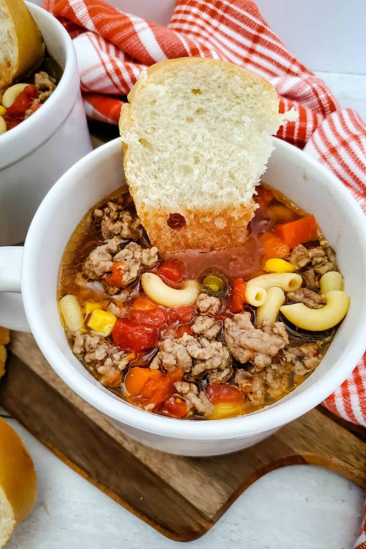 A bowl of crockpot beef macaroni soup with a slice of garlic bread resting on the rim.