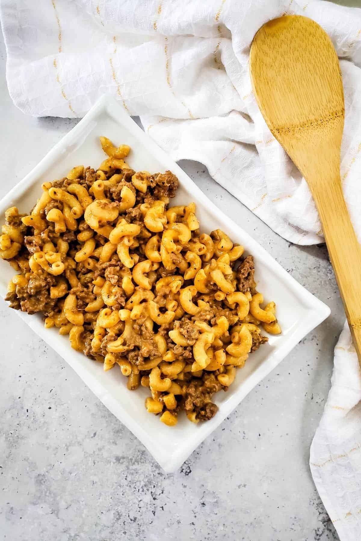A serving dish filled with cheesy burger macaroni, set on top of a cloth for a cozy presentation.