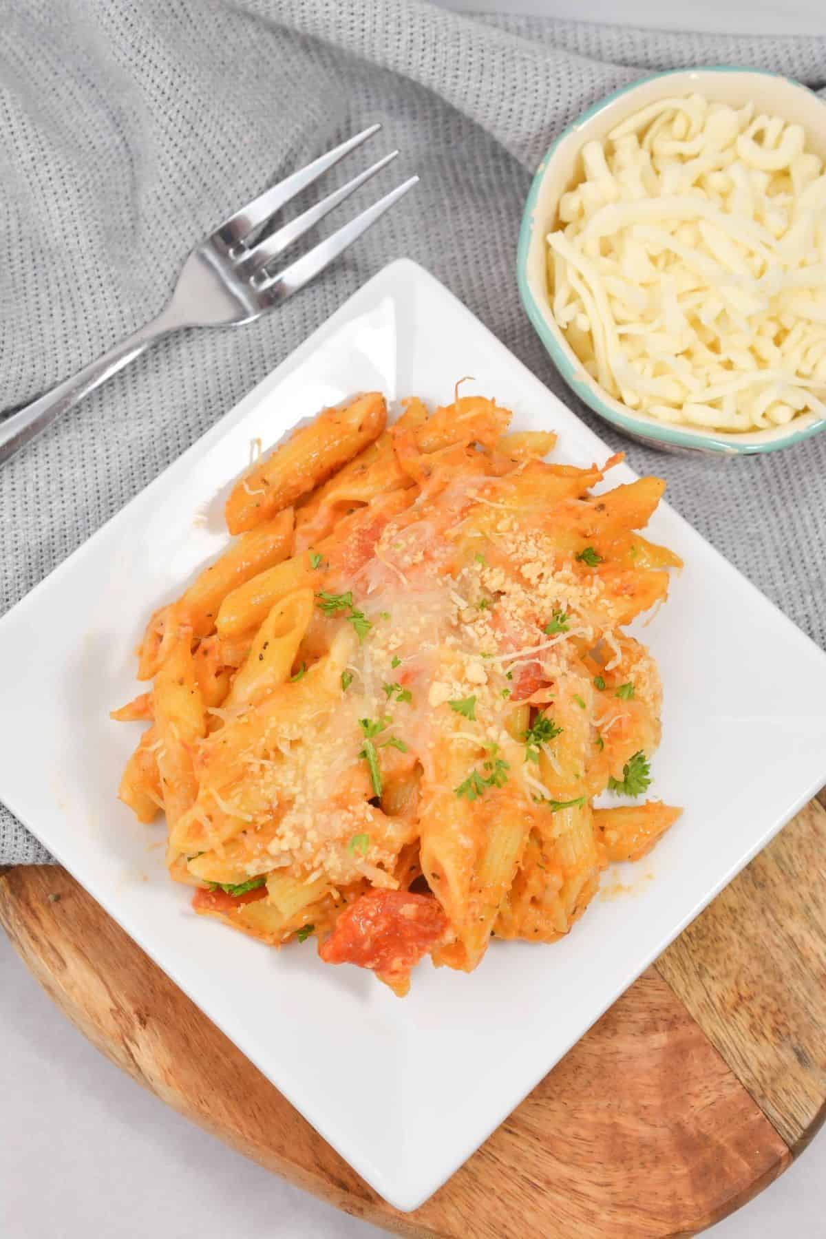A plate of pepperoni mac and cheese with a fork on the side, accompanied by a small bowl filled with shredded cheese.