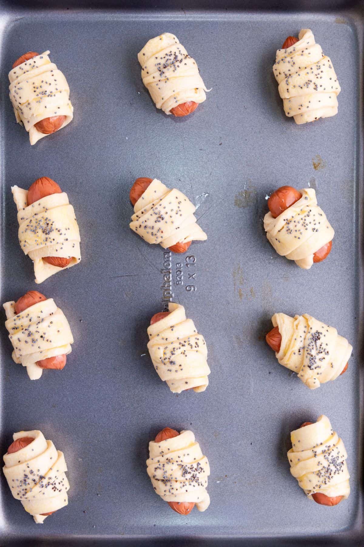 Sausages rolled in dough arranged on a parchment-lined baking sheet, ready for baking.