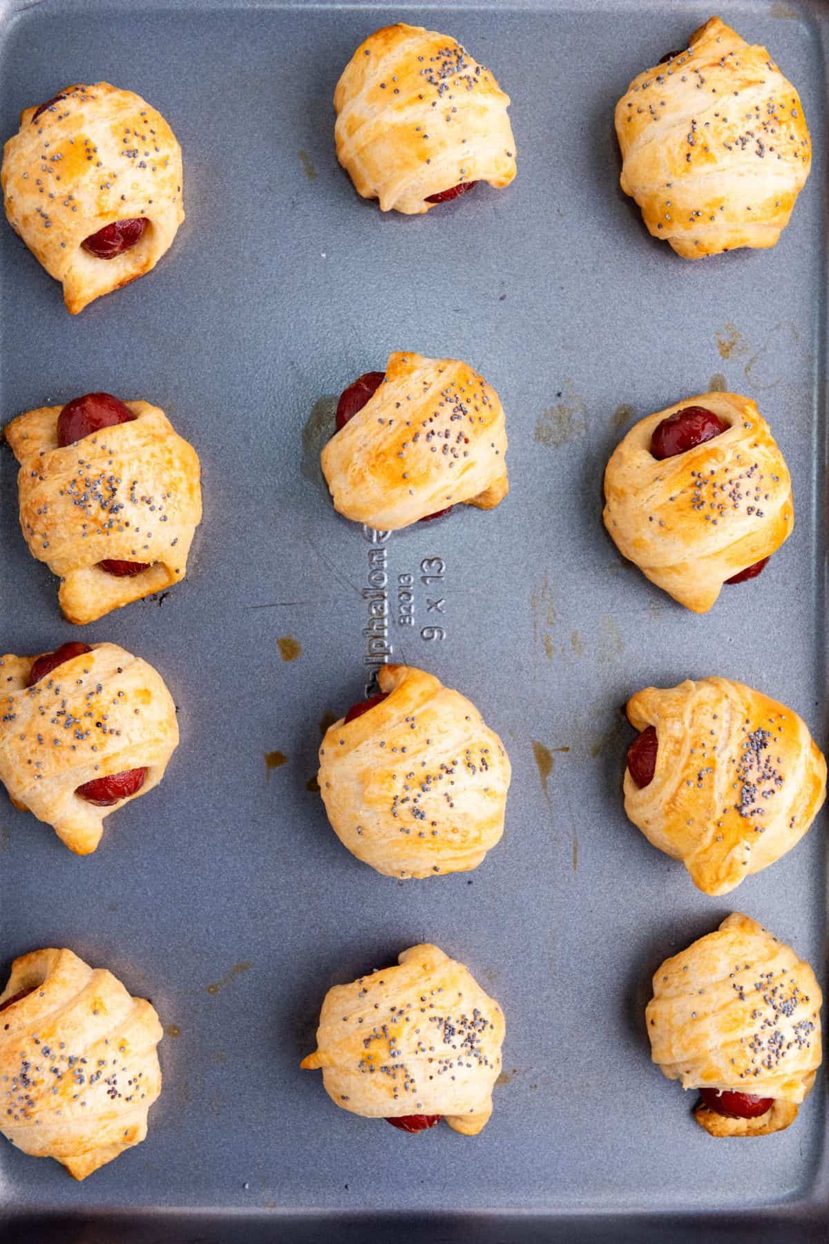 Freshly baked mini piggies in a blanket on a parchment-lined baking sheet, golden and ready to serve.