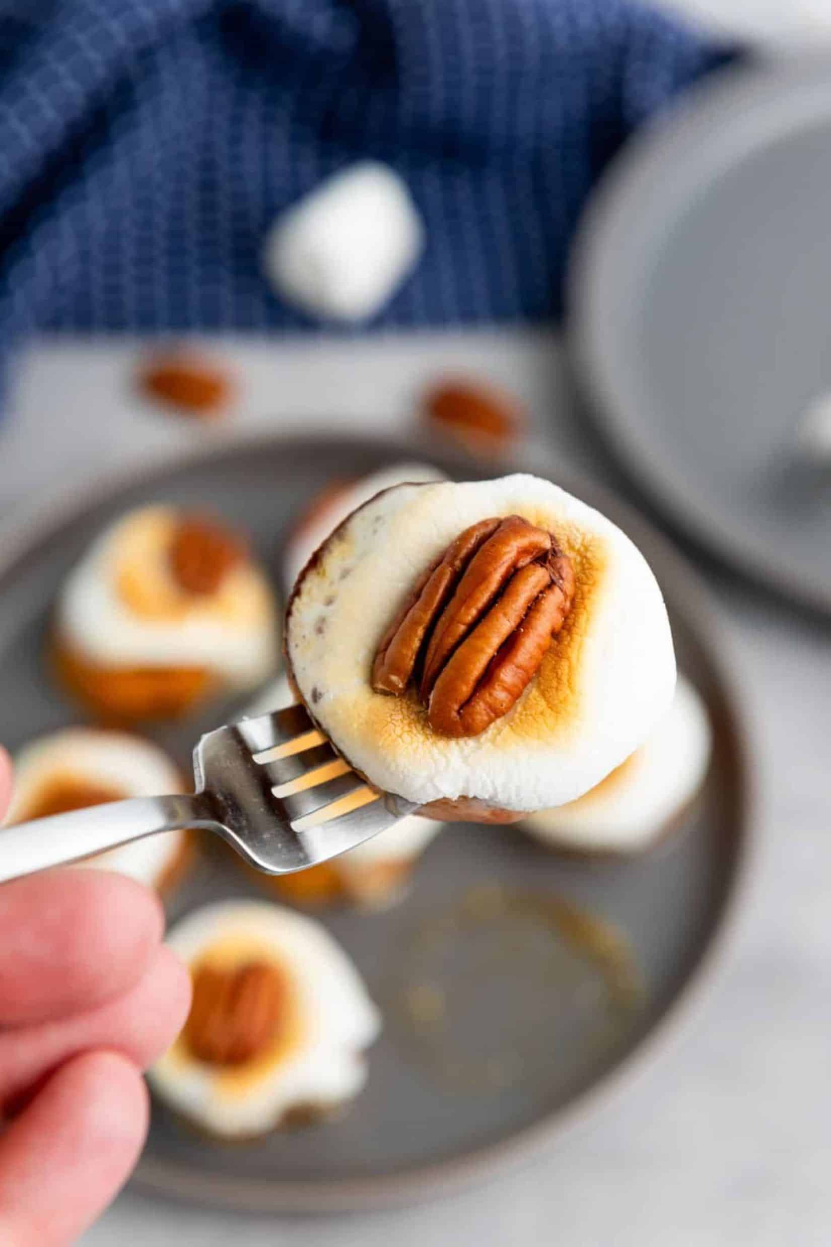 A person holding a fork lifting a baked sweet potato bite, with a plate full of more sweet potato bites blurred in the background.