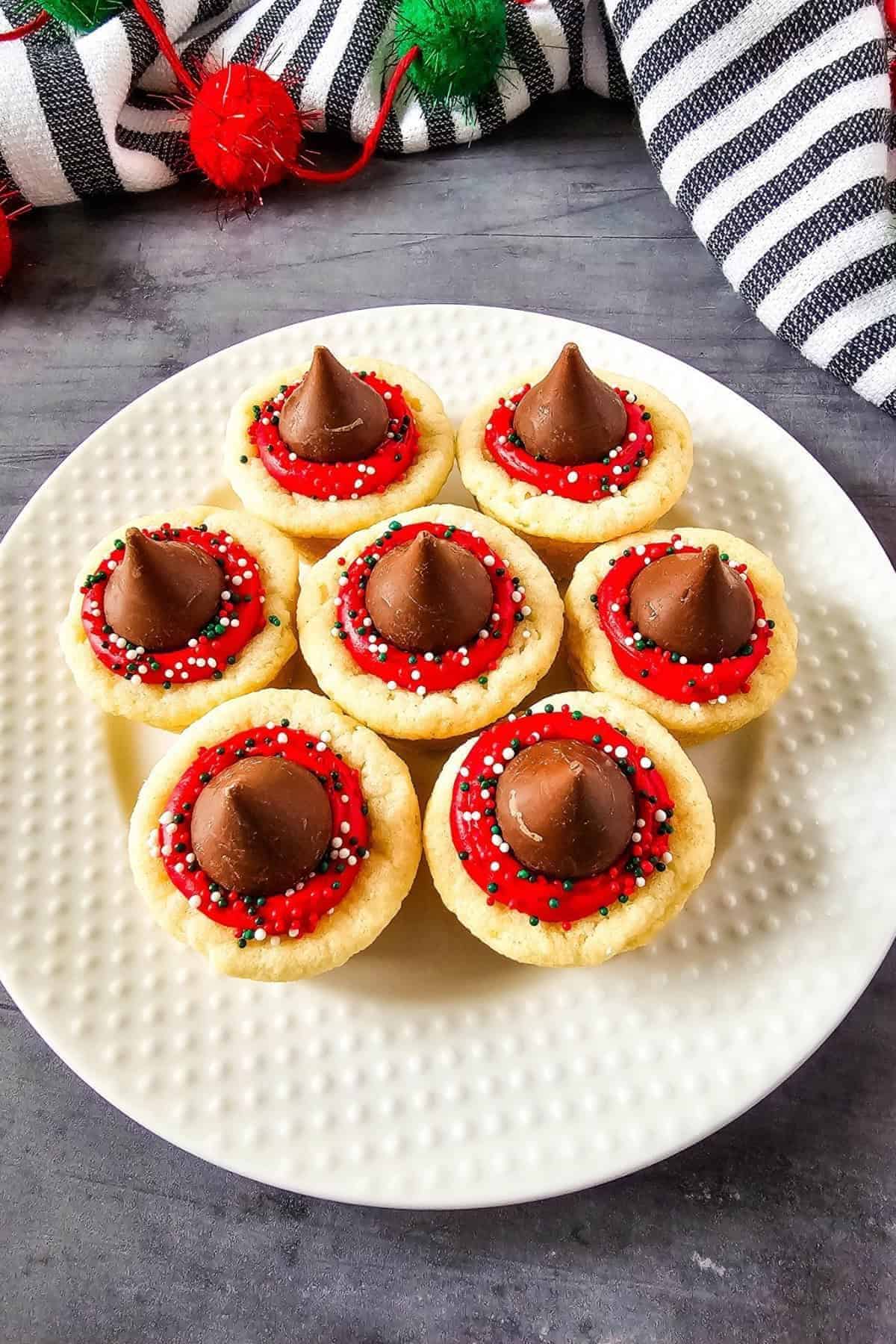 Christmas cookie cups topped with a chocolate kiss, arranged on a plate, showing their festive decorations and texture.